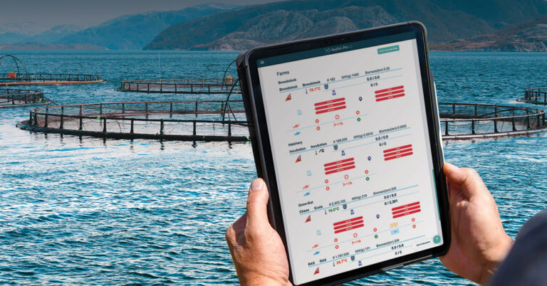 Person holding tablet displaying aquaculture farm monitoring software with fish pen locations and data overlaid on water with mountain backdrop.