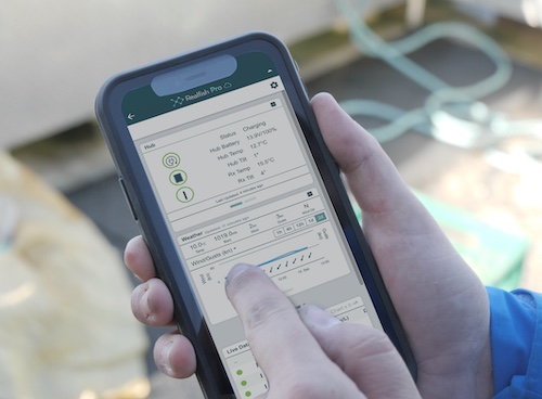 Person holding a smartphone displaying RealFish Pro app for aquaculture.