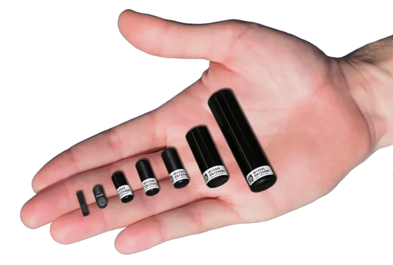 A human hand holds six small black cylindrical devices of increasing size, appearing to be electronic components or sensors with white labels.