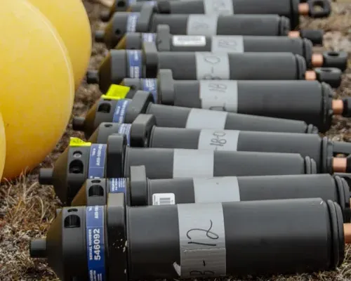 Multiple fine scale positioning gray cylindrical devices with numbered labels arranged in rows on ground, with yellow circular objects visible on the left side.