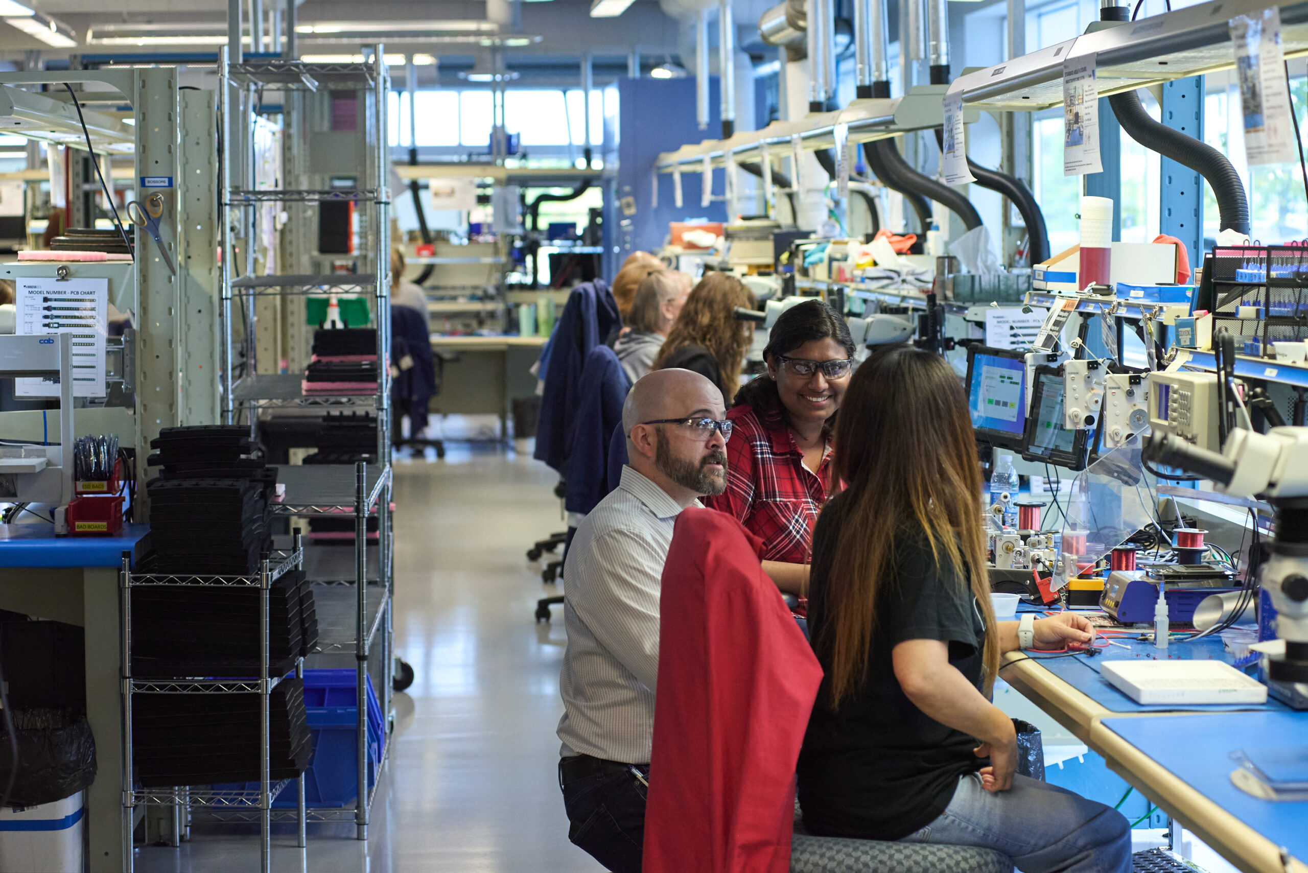 People working together at workstations in a modern laboratory or technical facility with equipment and shelving.